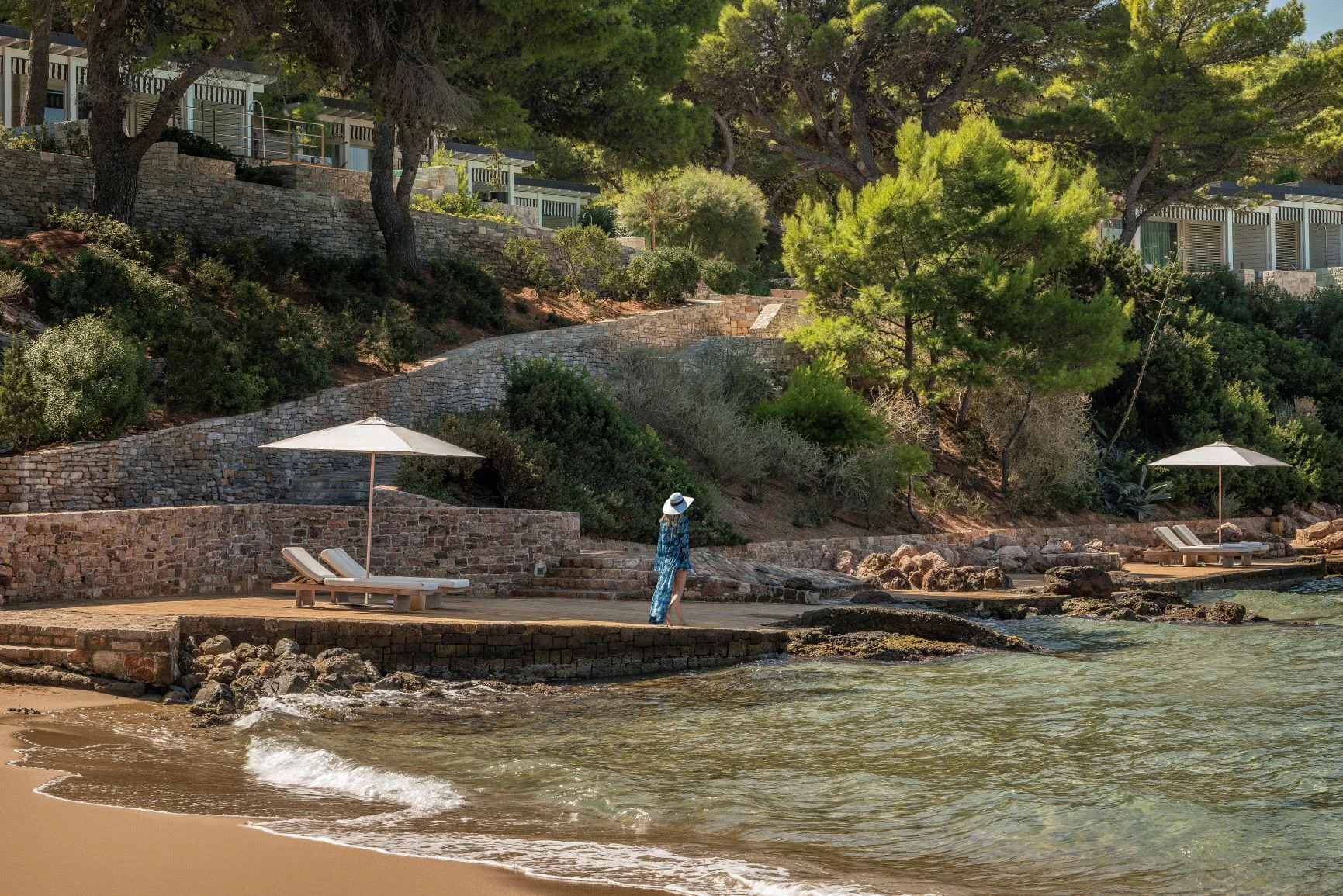 Pine-shaded waterfront terraces and a small sandy cove at Four Seasons Astir Palace