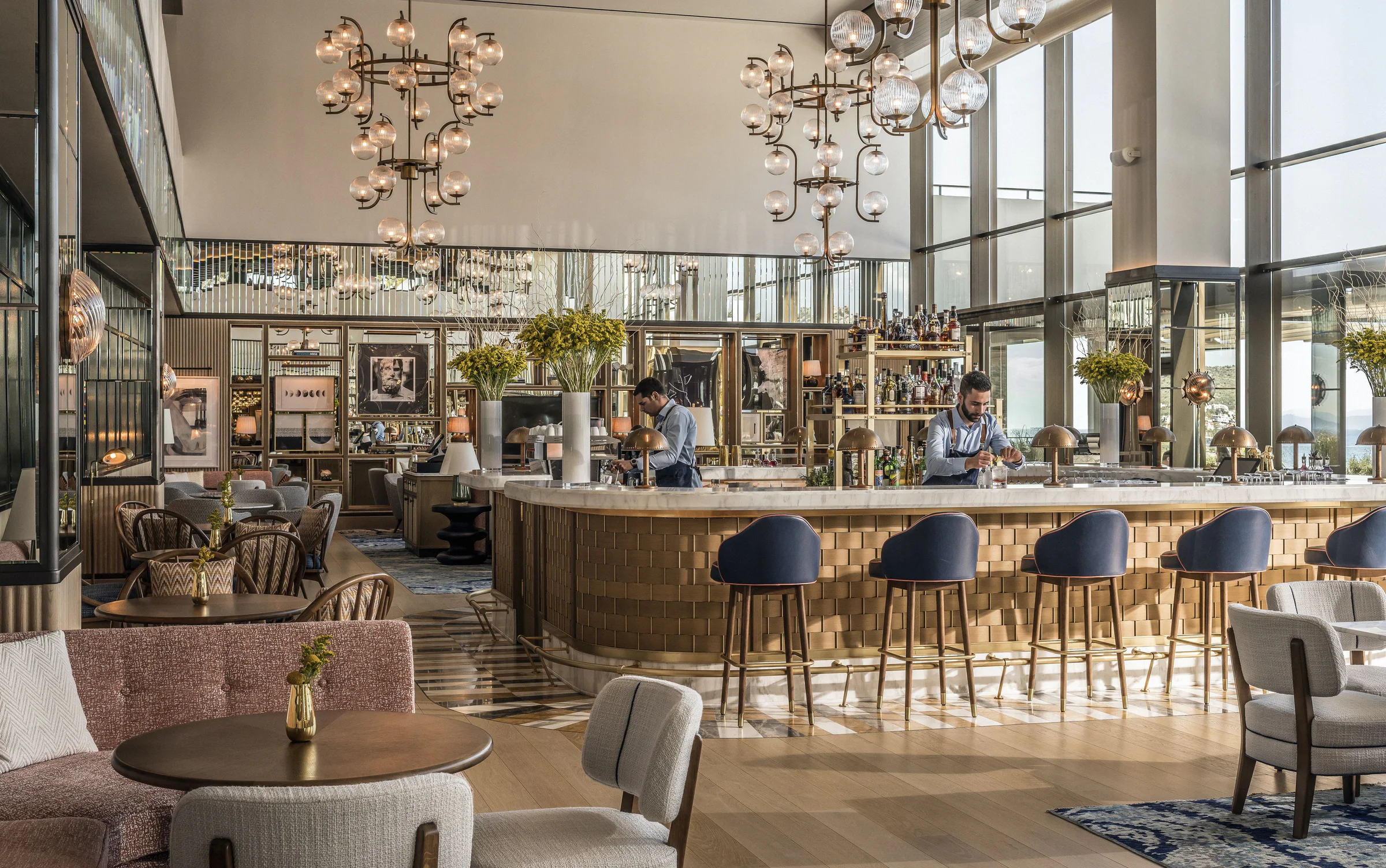 Marble and brass resort bar beneath sculptural glass lights at Astir Palace