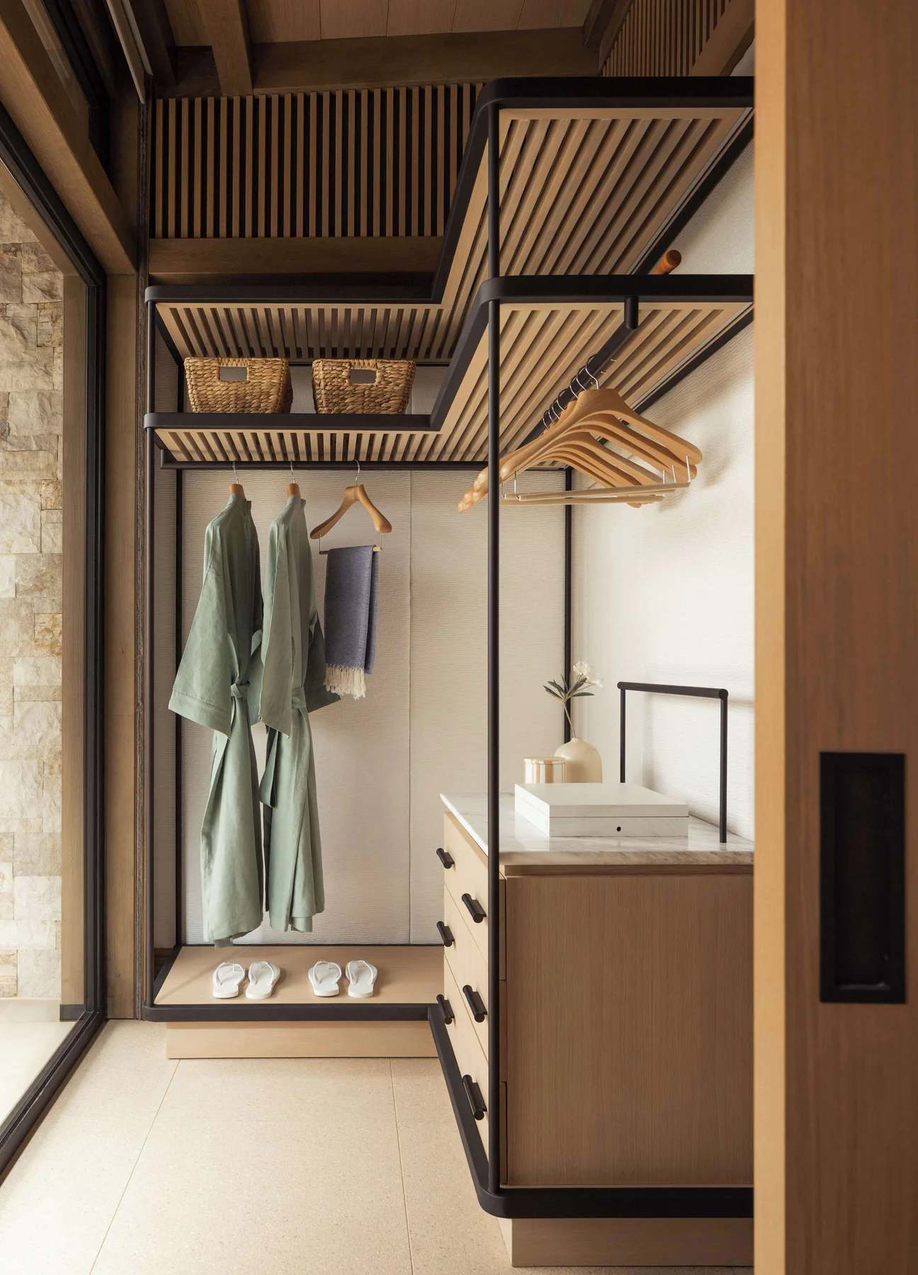 Timber and stone walk-in wardrobe with robes and guest slippers