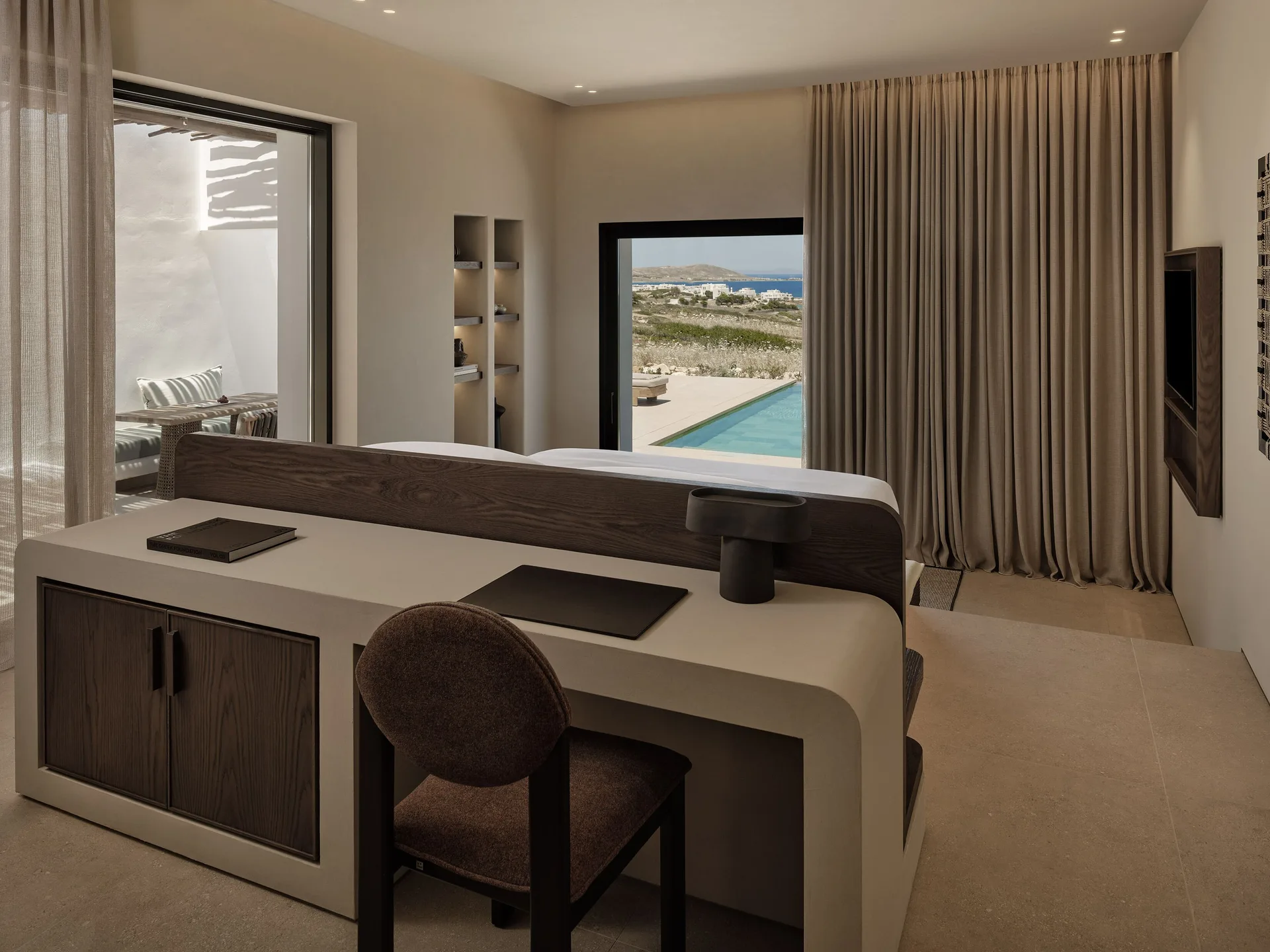 Calm private-pool suite with a desk, shaded seating and views towards the coast